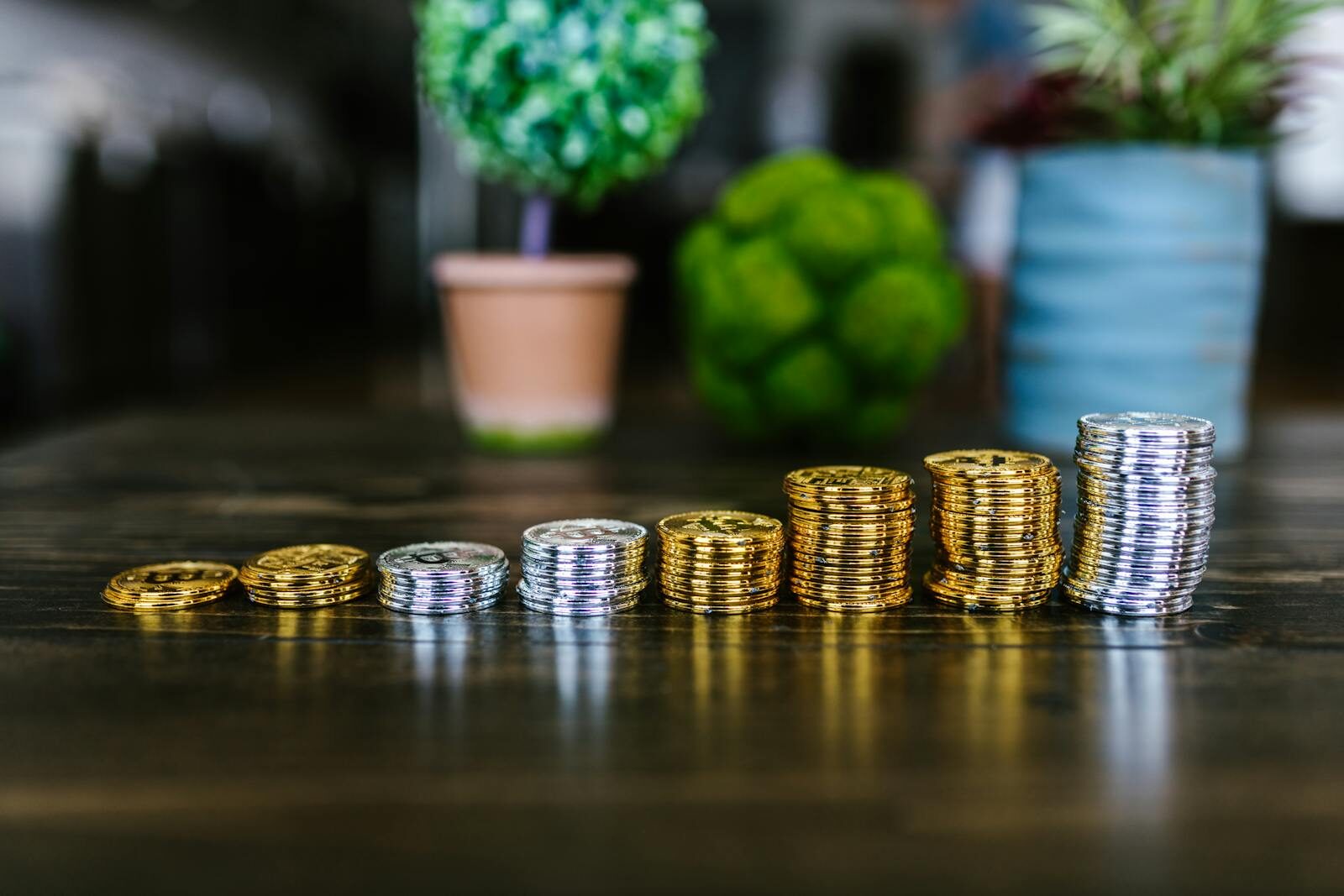 Close-up of stacked gold and silver bitcoins on a wooden table with plants in the background.